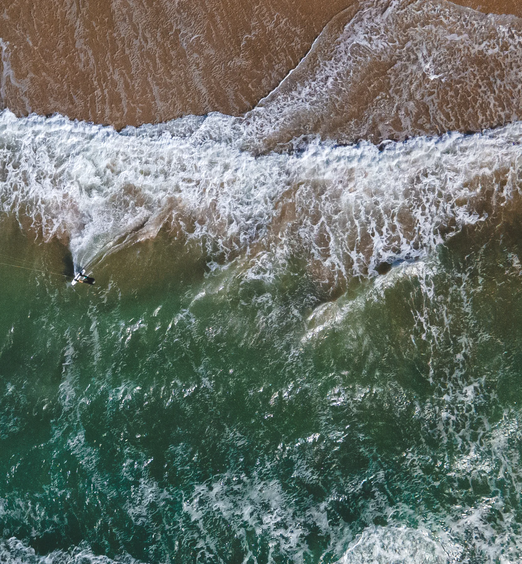 © Lasse Diercks Big teal Ocean waves on beach from birds-eye view.